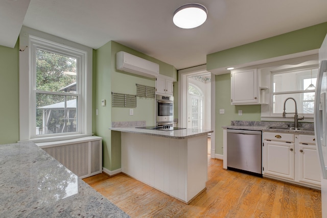 kitchen featuring radiator, white cabinets, light hardwood / wood-style flooring, stainless steel appliances, and a wall unit AC