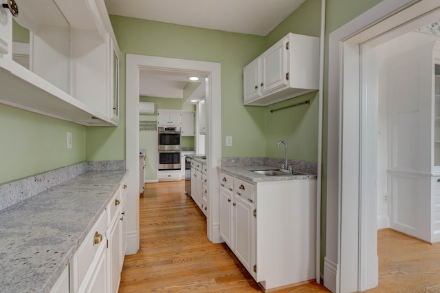 kitchen featuring light stone countertops, double oven, sink, white cabinets, and light hardwood / wood-style floors