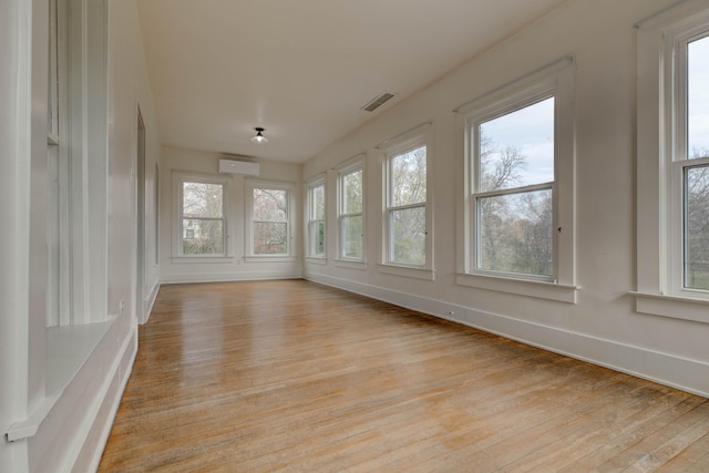 unfurnished sunroom with a wall mounted air conditioner and a healthy amount of sunlight