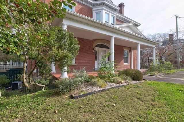 view of front of house featuring covered porch, central AC unit, and a front yard