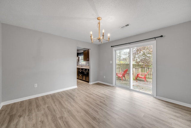 empty room featuring a chandelier, sink, a textured ceiling, and light hardwood / wood-style flooring