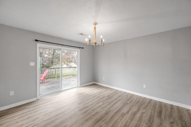 empty room with an inviting chandelier, a textured ceiling, and light wood-type flooring