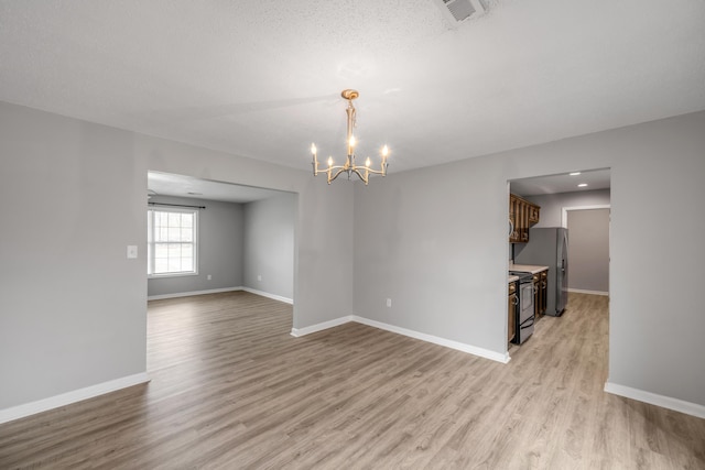 spare room with a textured ceiling, an inviting chandelier, and light hardwood / wood-style flooring