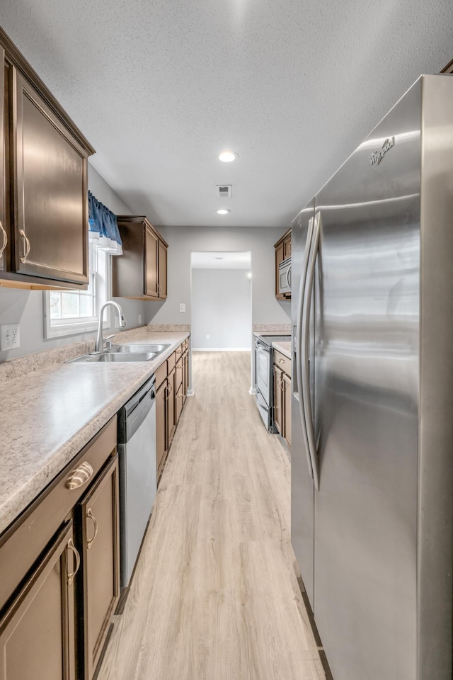 kitchen with sink, stainless steel appliances, light hardwood / wood-style floors, and a textured ceiling