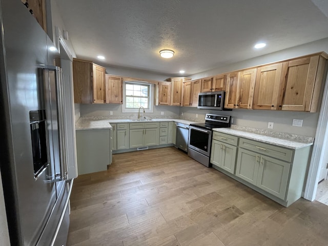 kitchen with appliances with stainless steel finishes, sink, green cabinets, and light hardwood / wood-style flooring