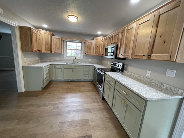 kitchen featuring stainless steel appliances, sink, a textured ceiling, and light wood-type flooring