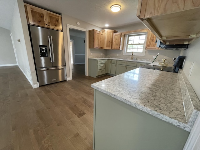 kitchen with sink, light stone counters, high end refrigerator, range, and hardwood / wood-style flooring