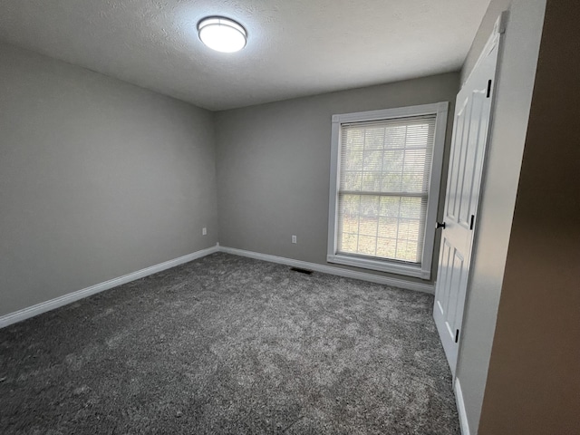 empty room with dark carpet and a textured ceiling