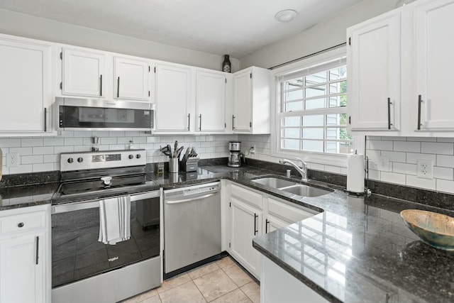 kitchen featuring white cabinetry, sink, dark stone counters, light tile patterned floors, and appliances with stainless steel finishes