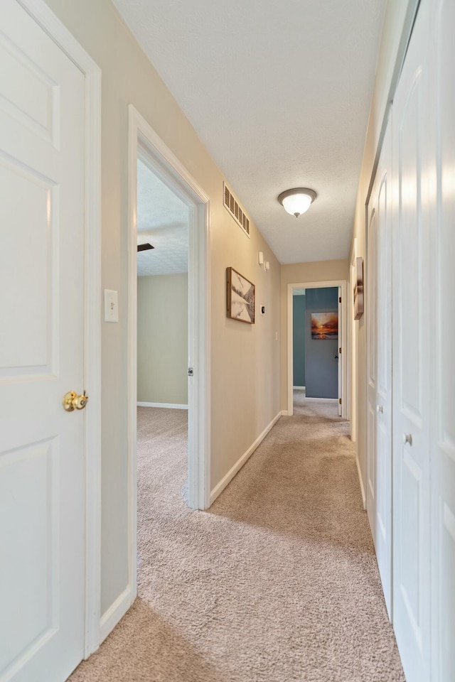 corridor with light colored carpet and a textured ceiling