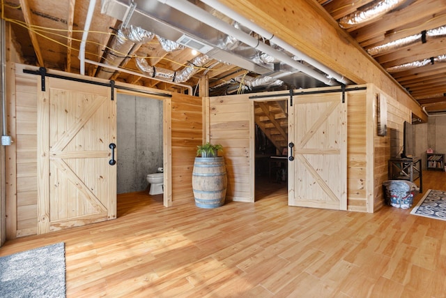 basement with a barn door, wood walls, and hardwood / wood-style flooring