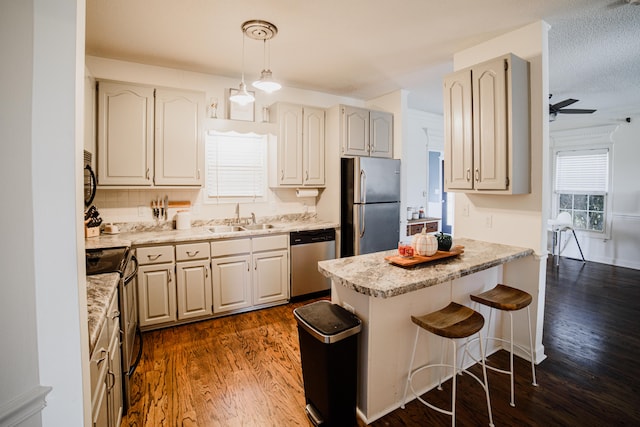 kitchen featuring a kitchen bar, sink, ceiling fan, appliances with stainless steel finishes, and dark hardwood / wood-style flooring