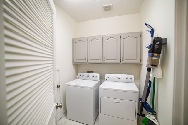 clothes washing area with washer and dryer, cabinets, and a textured ceiling