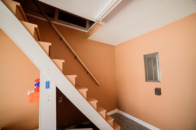 stairway with a textured ceiling and electric panel