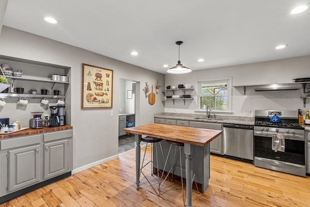 kitchen with a kitchen bar, sink, butcher block countertops, hanging light fixtures, and stainless steel appliances