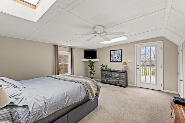 carpeted bedroom featuring multiple windows, access to exterior, vaulted ceiling with skylight, and ceiling fan