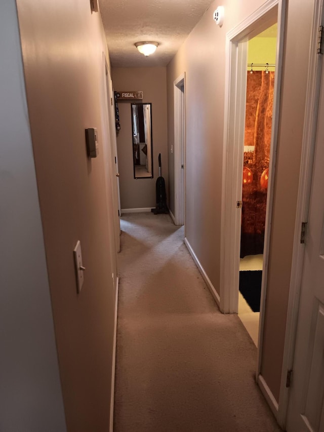 hallway with light carpet, a textured ceiling, and baseboards