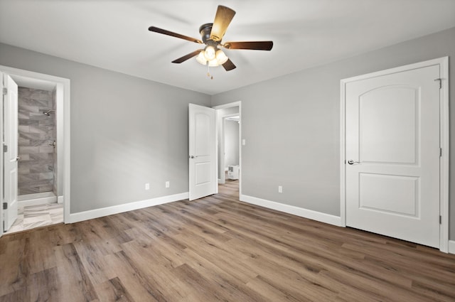 unfurnished bedroom with ceiling fan, ensuite bathroom, and wood-type flooring