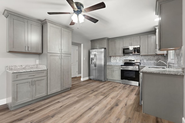 kitchen featuring gray cabinetry, sink, light hardwood / wood-style flooring, light stone countertops, and stainless steel appliances