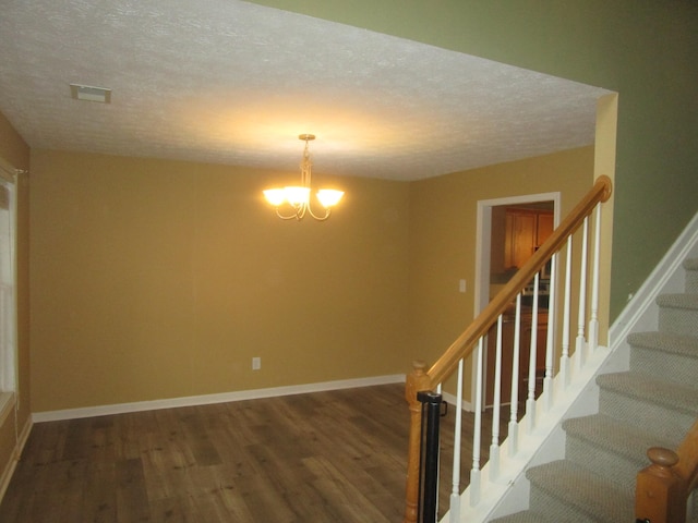 stairs featuring hardwood / wood-style floors, a textured ceiling, and a notable chandelier