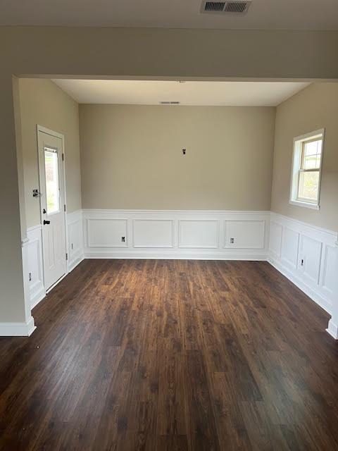 spare room with dark wood-style floors, a wainscoted wall, and visible vents