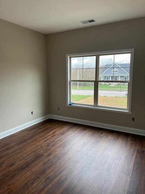 unfurnished room with dark wood-style floors, visible vents, and baseboards