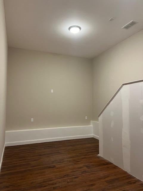 empty room featuring dark wood-type flooring, visible vents, and baseboards