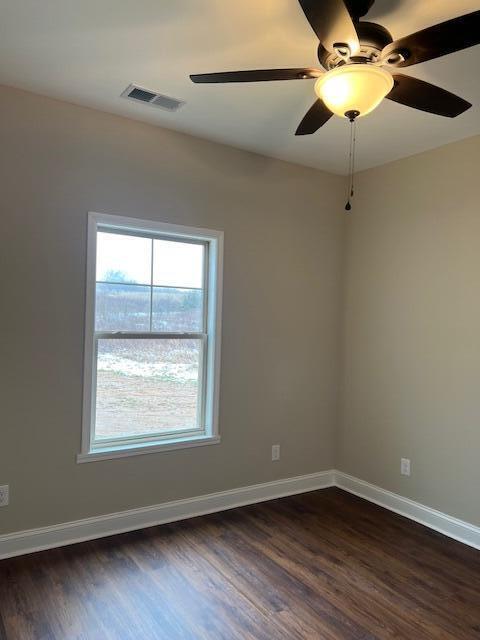 empty room featuring dark wood-type flooring, visible vents, and baseboards