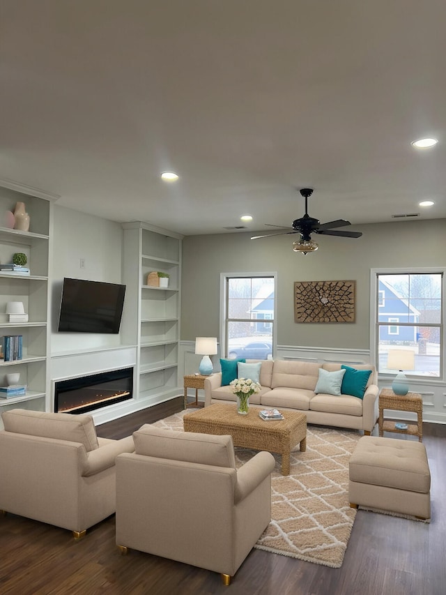 living room featuring built in shelves, recessed lighting, dark wood-type flooring, visible vents, and a glass covered fireplace