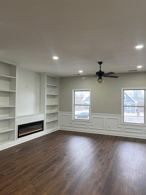 unfurnished living room with recessed lighting, a wainscoted wall, dark wood-type flooring, built in features, and a glass covered fireplace