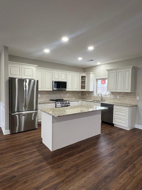 kitchen with a kitchen island, appliances with stainless steel finishes, dark wood-type flooring, white cabinetry, and a sink