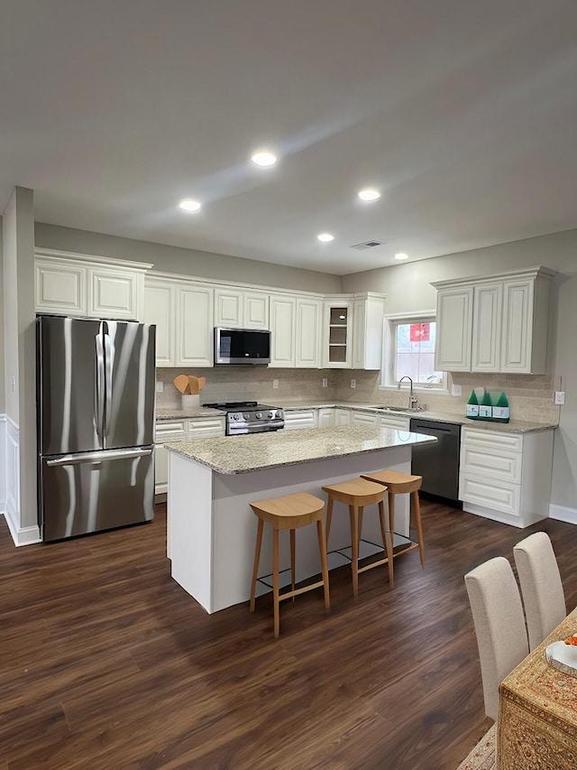 kitchen featuring white cabinets, glass insert cabinets, appliances with stainless steel finishes, a center island, and a sink