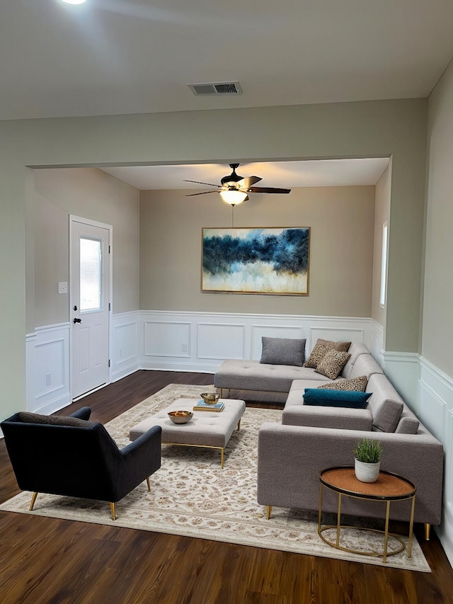 living room with dark wood-style floors, visible vents, and wainscoting