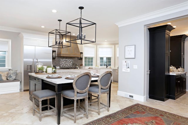 kitchen featuring built in fridge, a center island, decorative light fixtures, a kitchen bar, and crown molding