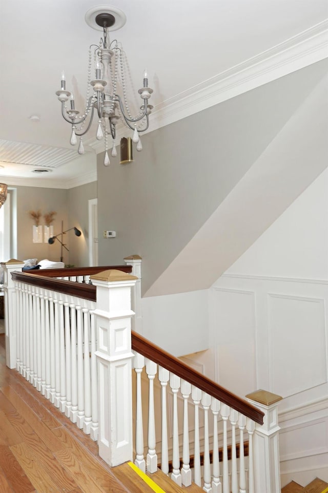 stairs with wood-type flooring, ornamental molding, and a chandelier