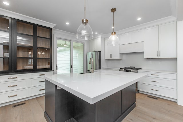 kitchen featuring crown molding, appliances with stainless steel finishes, a kitchen island with sink, and decorative light fixtures