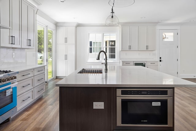 kitchen with a center island with sink, sink, hanging light fixtures, light stone countertops, and stainless steel appliances