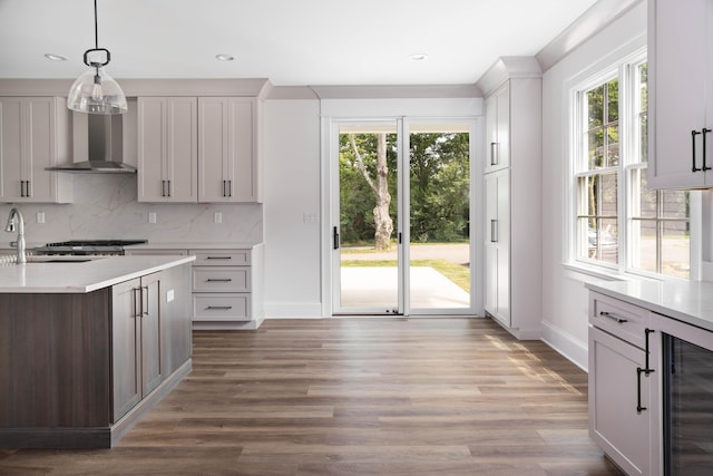 kitchen featuring pendant lighting, a wealth of natural light, wall chimney range hood, wine cooler, and tasteful backsplash