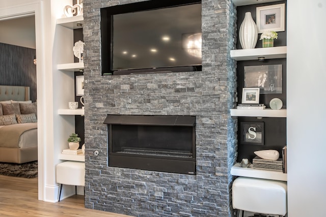 living room featuring wood-type flooring, built in features, and a stone fireplace