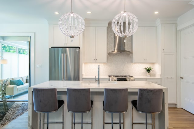 kitchen featuring stainless steel fridge, wall chimney range hood, an inviting chandelier, and white cabinetry