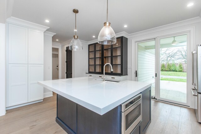 kitchen with pendant lighting, appliances with stainless steel finishes, sink, light wood-type flooring, and a center island with sink