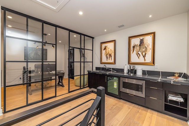 kitchen with sink, beverage cooler, stainless steel microwave, and light wood-type flooring