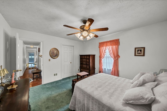 bedroom featuring dark colored carpet, a textured ceiling, and ceiling fan