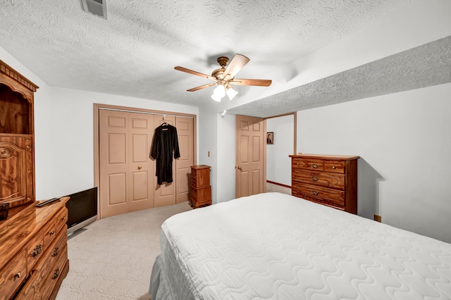 bedroom featuring ceiling fan, a closet, light colored carpet, and a textured ceiling