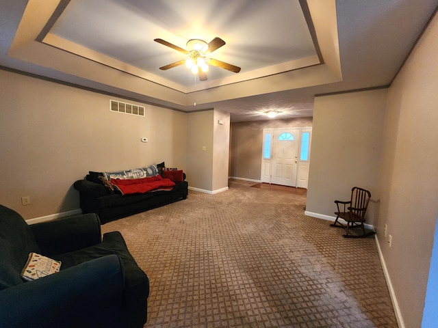 living room with a raised ceiling, ceiling fan, and carpet flooring