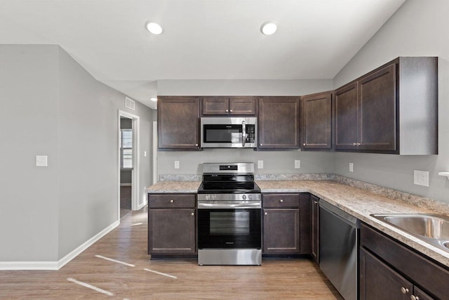 kitchen featuring appliances with stainless steel finishes, dark brown cabinets, sink, and light wood-type flooring