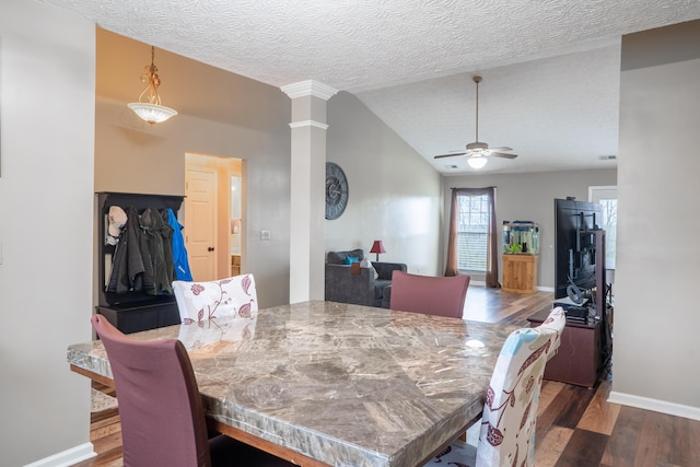 dining space featuring dark wood-type flooring, vaulted ceiling, ceiling fan, a textured ceiling, and decorative columns