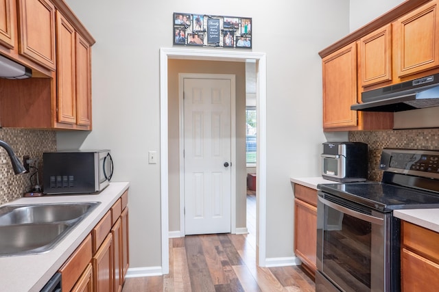 kitchen featuring backsplash, sink, range hood, appliances with stainless steel finishes, and light hardwood / wood-style floors