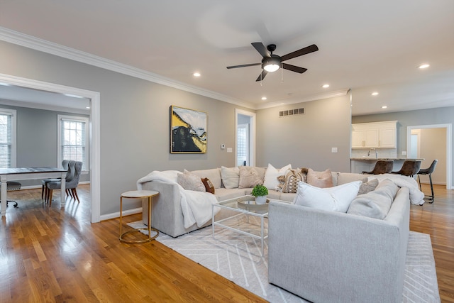 living room featuring light wood-type flooring, ceiling fan, and ornamental molding