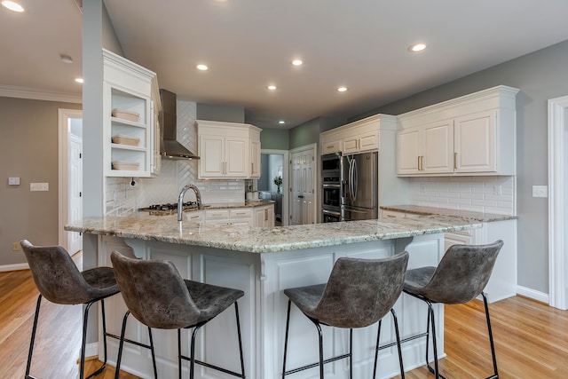 kitchen featuring light stone countertops, appliances with stainless steel finishes, kitchen peninsula, and wall chimney range hood